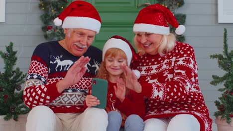 Smiling-grandparents-and-granddaughter-waving-during-video-call-on-smartphone-at-Christmas-reunion