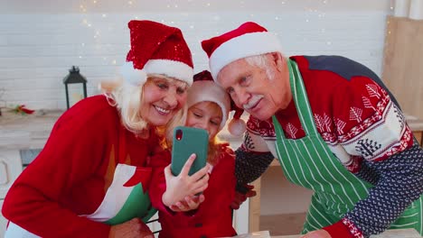 Senior-grandparents-with-granddaughter-kid-taking-selfie-photo-on-mobile-phone-at-Christmas-kitchen