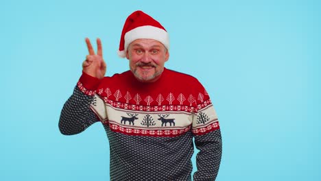 Positive-man-in-Christmas-sweater-with-deers-waves-hand-palm-in-hello-gesture-welcomes-someone