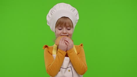 Child-girl-5-6-years-old-dressed-in-apron-like-chef-cook-eating-tasty-bun-on-chroma-key-background