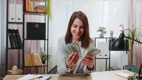 Smiling-businesswoman-counting-cash-money-dollar-checking-salary-enjoy-richness-at-home-office-table