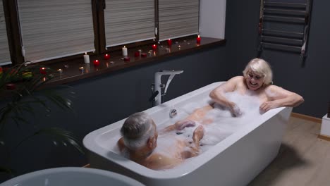 Senior-couple-grandfather-and-grandmother-is-taking-foamy-bath-drinking-red-wine-in-luxury-bathroom