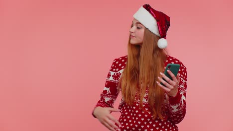 Girl-in-Christmas-Santa-sweater-with-mobile-phone-showing-pointing-empty-place,-advertising-area