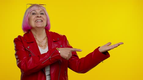 Mature-grandmother-showing-thumbs-up-and-pointing-empty-place,-advertising-area-for-commercial-text