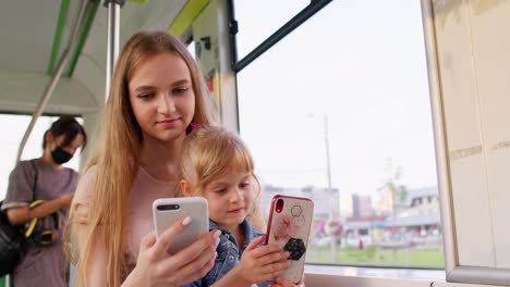 Child-girl-with-mother-using-smartphone-chatting-texting-in-social-media,-public-transport-bus,-tram