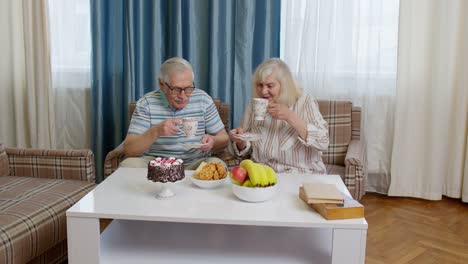 Senior-couple-holding-drinking-tea-talking,-laughing,-smiling,-kissing,-sitting-on-sofa-at-home