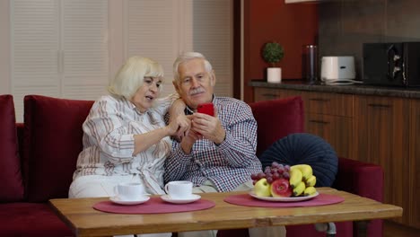 Senior-old-couple-grandparents-talking-and-using-digital-mobile-phone-at-home.-Online-shopping
