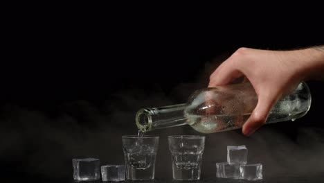 Barkeeper-Gießt-Zwei-Shots-Wodka-Mit-Eiswürfeln-Aus-Der-Flasche-In-Gläser-Auf-Schwarzem-Hintergrund