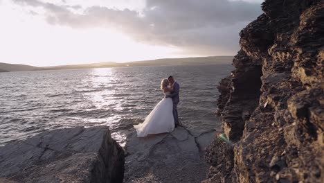Newlyweds-couple-on-a-mountainside-by-the-sea.-Sunset.-Groom-and-bride