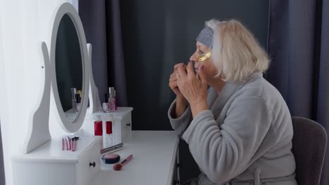 Old-senior-woman-grandmother-taking-care-of-skin-near-eyes-and-wrinkles,-putting-makeup-on-at-home