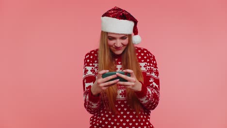Worried-girl-in-Christmas-sweater,-hat-enthusiastically-playing-racing-video-games-on-mobile-phone
