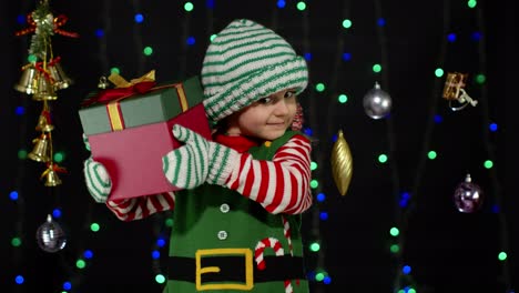 Kind-Im-Weihnachtselfenkostüm-Des-Weihnachtsmannes,-Das-Ein-Geschenk-Mit-Einer-Geschenkbox-Und-Einer-Schleife-Hält