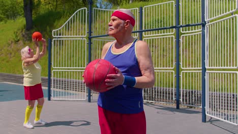 Senior-man-grandfather-posing-with-ball,-looking-at-camera-outdoors-on-basketball-playground-court