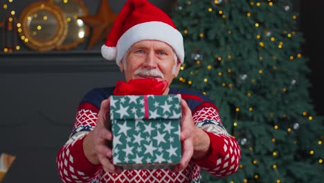 Senior-grandfather-in-New-Year-sweater-and-hat-presenting-Christmas-gift-box,-holidays-at-home