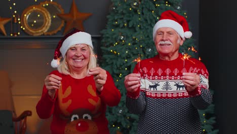 Senior-family-couple-in-festive-sweaters-holding-bengal-lights-enjoying-Christmas-eve-at-home-room