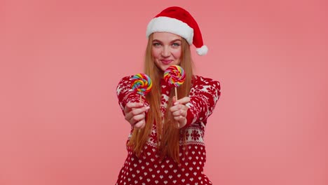 Joyful-girl-in-red-Christmas-sweater,-hat-presenting-candy-striped-lollipops,-stretches-out-hands