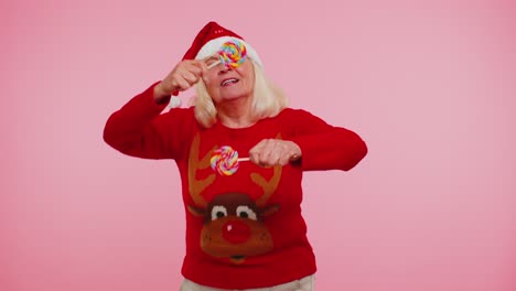 Senior-grandmother-in-Christmas-sweater-holding-candy-striped-lollipops,-dancing-making-silly-faces