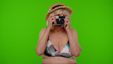 Senior-woman-tourist-photographer-in-swimsuit-taking-photos-on-retro-camera,-smiling-on-chroma-key