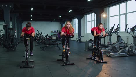 Group-of-girls-performs-aerobic-training-workout-cardio-routine-on-bike-simulators,-cycle-training