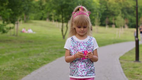 Girl-playing-with-pop-it-sensory-anti-stress-hand-spinner-squishy-bubbles-toy-while-walking-in-park