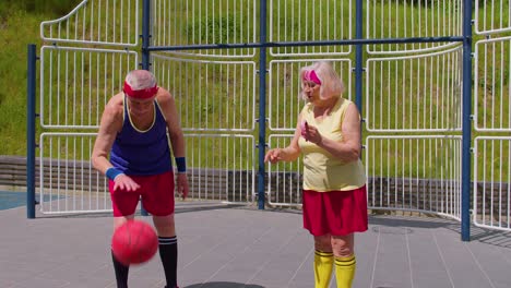 Senior-woman-coach-teaching-grandfather-with-basketball-dribbling-exercise-with-ball-on-playground