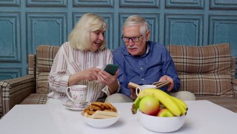 Abuelos-De-Pareja-De-Ancianos-Hablando-Y-Usando-Teléfonos-Móviles-Digitales-En-Casa.-Las-Compras-En-Línea