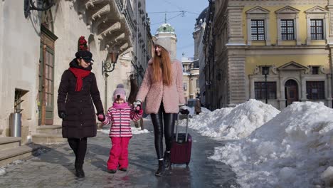 Sisters-tourists-travelers-walking-with-a-suitcase-on-snowy-city-street,-enjoying-time-together