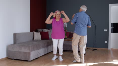 Senior-couple-dancing-laughing-at-home.-Grandparents-relaxing-having-fun-celebrating-anniversary