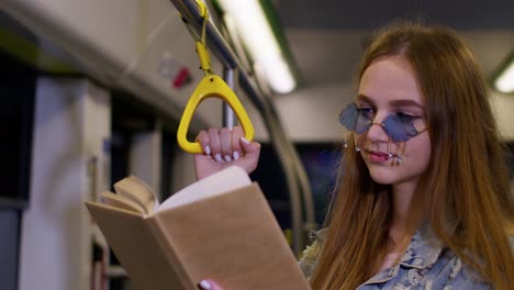 Portrait-of-attractive-young-adult-woman-stay-at-empty-subway-train-and-reading-interesting-book