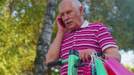 Elderly-old-grandfather-man-on-electric-scooter-with-colorful-shopping-bags-talking-on-mobile-phone