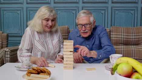 Senior-couple-grandfather,-grandmother-resting-on-sofa,-playing-game-with-wooden-blocks-at-home