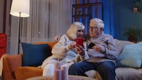Senior-family-couple-with-smartphone-at-home,-making-online-shopping-with-credit-plastic-bank-cards