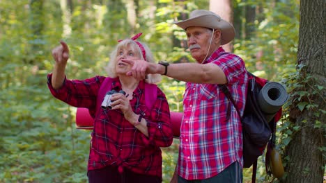 Senior-old-grandmother-grandfather-tourists-hiking,-traveling,-exploring-forest-using-binoculars