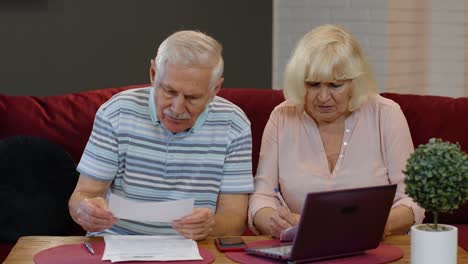 Senior-couple-checking-calculating-bills-bank-loan-payment-doing-paperwork-discuss-unpaid-debt-taxes