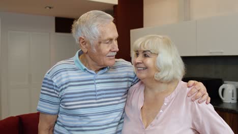 Senior-family-couple-hugging,-laughing,-smiling-looking-at-camera-during-coronavirus-lockdown