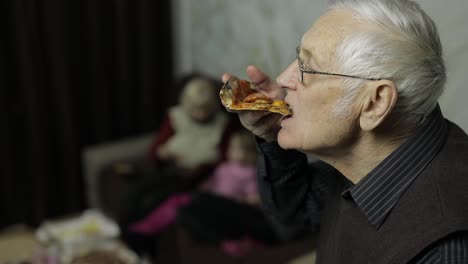Beautiful-elderly-man-in-glasses-eats-pizza.-His-family-in-background