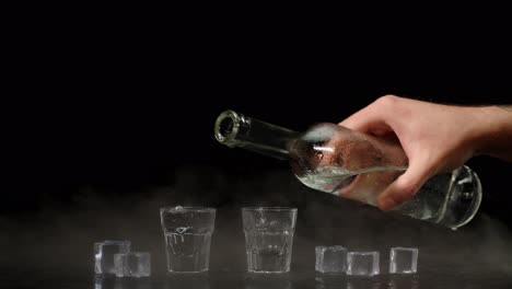 Two-hands-with-glasses-of-vodka-making-cheers,-raising-toast-on-black-background-with-ice-cubes