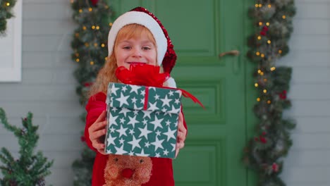 Joyful-toddler-child-girl-kid-in-red-sweater-presenting-one-Christmas-gift-box,-stretches-out-hands