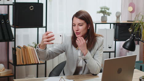 Geschäftsfrau,-Die-Ein-Smartphone-Verwendet,-Um-Einen-Videoanruf-Für-Soziale-Medien-Aufzunehmen,-Posiert-Lächelnd-Am-Bürotisch