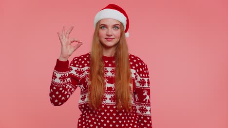 Adult-girl-in-Christmas-sweater-looking-approvingly-at-camera-showing-ok-gesture,-like-sign-positive