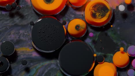 Top-view-movement-of-black-orange-oil-ink-drops-bubbles,-multicolored-artistic-paint-background