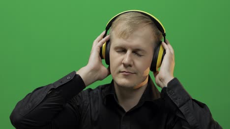 Guy-listens-to-music-in-wireless-yellow-headphones-and-dances.-Green-screen