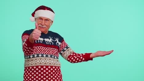 Großvater-Im-Weihnachtspullover-Mit-Hirschen-Zeigt-Daumen-Nach-Oben-Und-Zeigt-Auf-Eine-Leere-Werbefläche