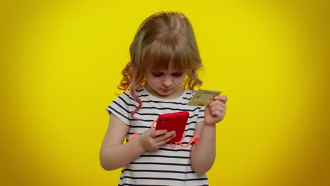 Little-teen-kid-child-girl-using-credit-bank-card-and-smartphone-while-purchases-online-shopping