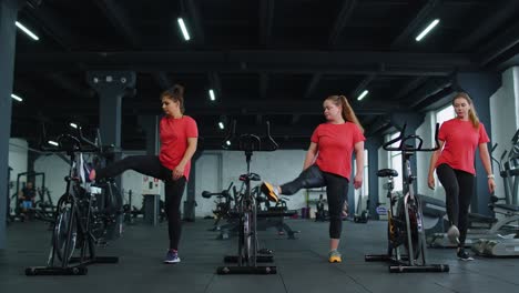 Healthy-Caucasian-group-of-women-exercising-stretching-on-stationary-cycling-machine-bike-in-gym
