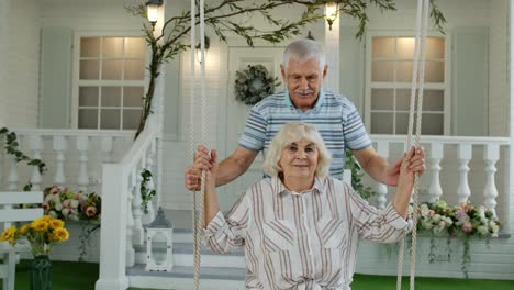 Senior-couple-together-in-front-yard-at-home.-Man-swinging-and-hugging-woman.-Happy-mature-family