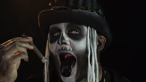 Scary-guy-in-carnival-costume-of-Halloween-skeleton-smoking-cigar,-making-faces,-showing-tongue