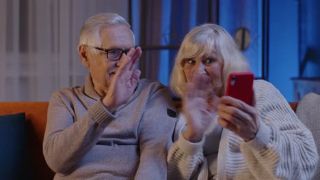 Lächelndes-älteres-Paar,-Großmutter-Und-Großvater,-Die-Auf-Dem-Sofa-Zu-Hause-Online-Einen-Videoanruf-Mit-Dem-Mobiltelefon-Tätigen