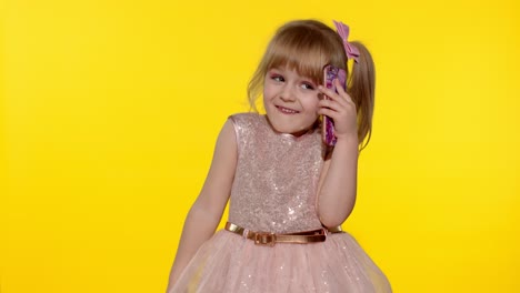 Lächelndes-Mädchen-Im-Alter-Von-5-6-Jahren,-Das-Auf-Gelbem-Hintergrund-Mit-Dem-Mobiltelefon-Spricht
