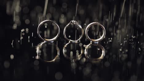 Wedding-and-engagement-rings-lying-on-dark-water-surface-shining-with-light